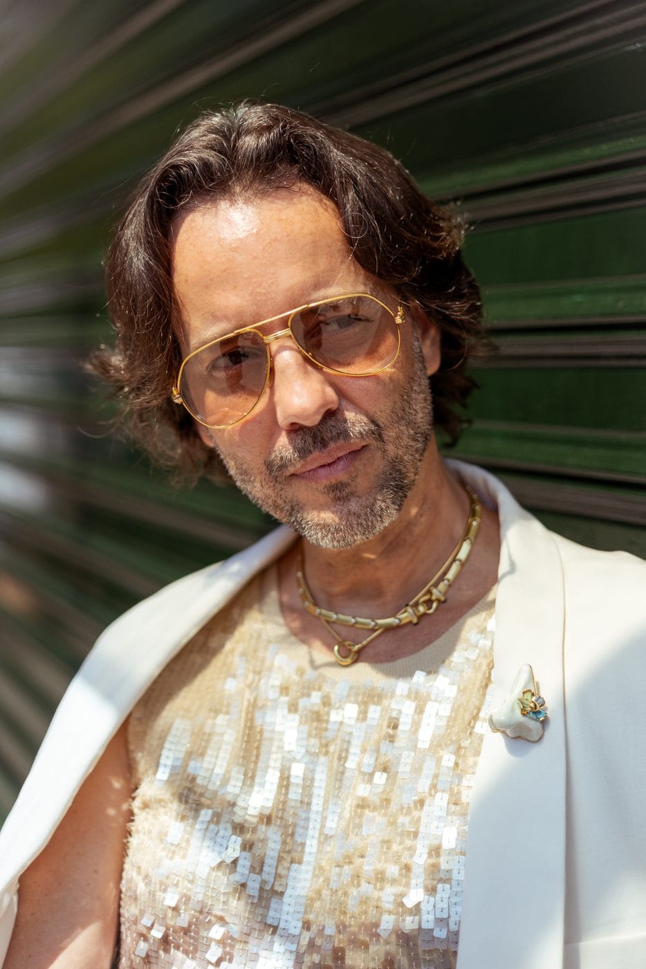 Man in gold aviators and a sequined tank against a green shutter, Paris