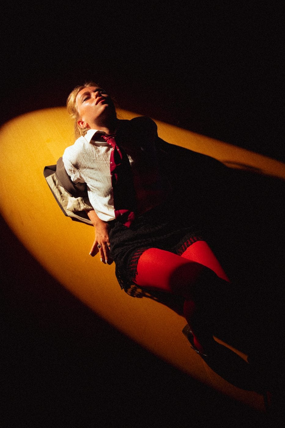 Figure lit by a single amber beam against black, red boots and a sweep of light across the floor, Amanda Black (@a.blck)