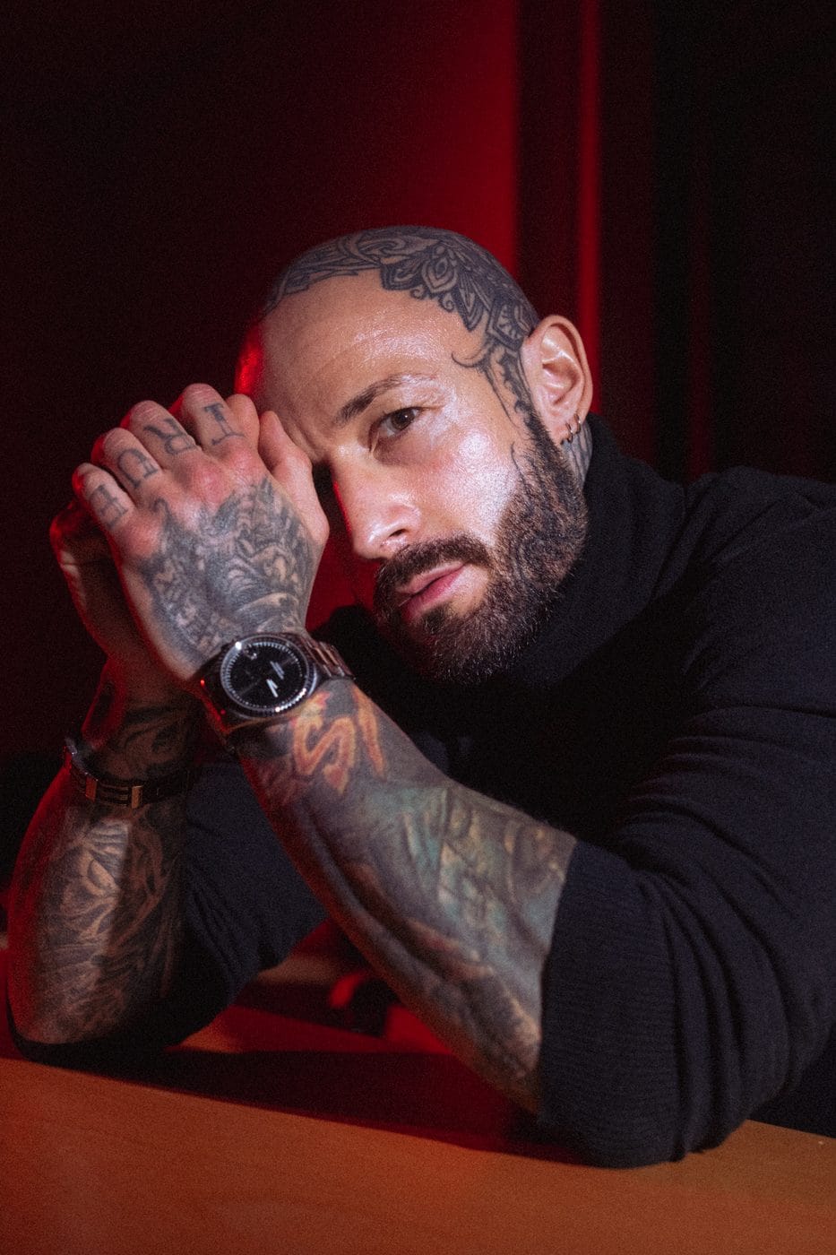 Portrait in low warm light, hand raised to the face, watch and rings catching the glow, Leon Krieft (@son.of.ink)