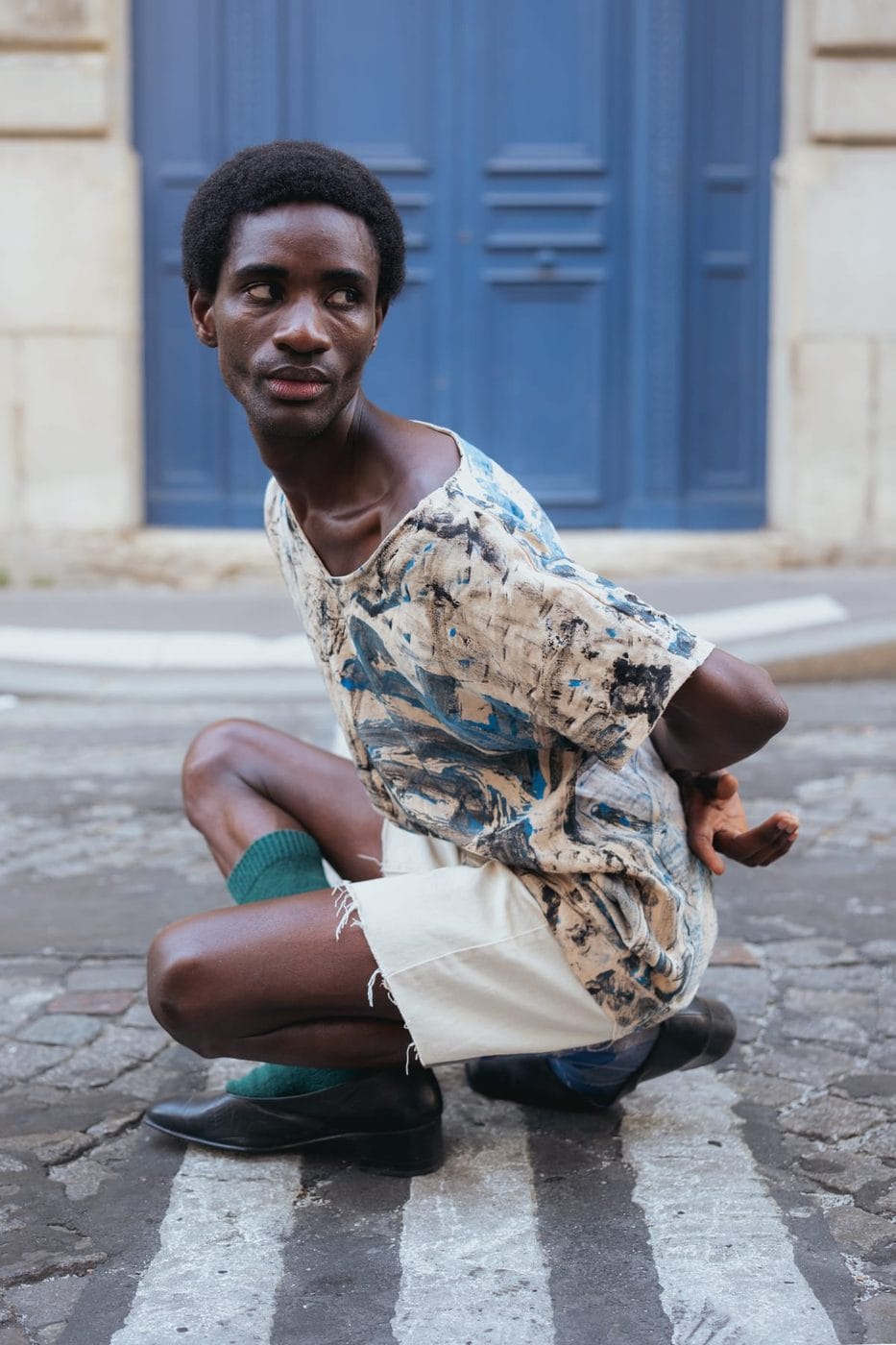 Man crouching in a patterned shirt in front of a blue door, @modelmodu