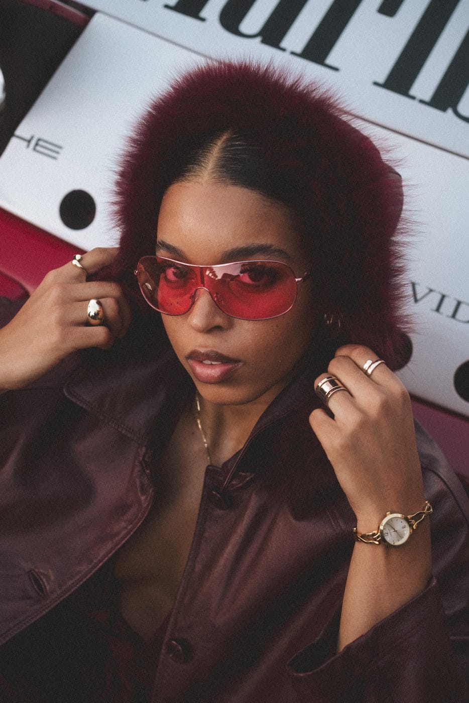 Portrait in red light, tinted sunglasses and a dark shearling collar, against a papered wall at night, Megan Bulose (@megan.bulose)