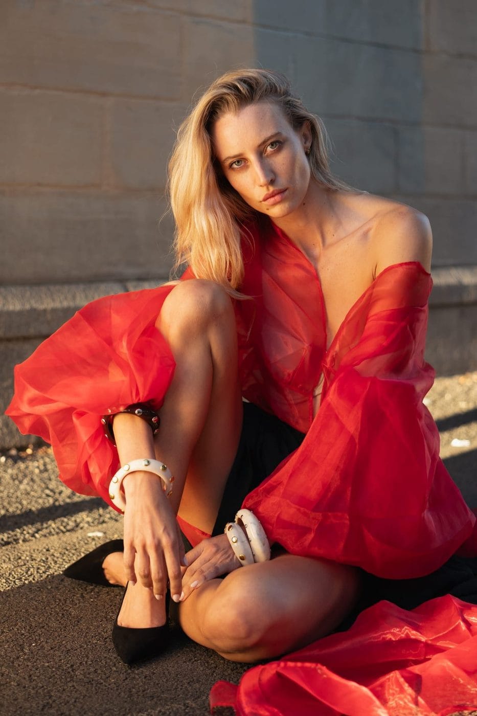 Woman seated on the pavement in a red organza dress, bare shoulders, Pascale Fairbairn (@pcfairbairn), Stylisme Yudith Hernandez