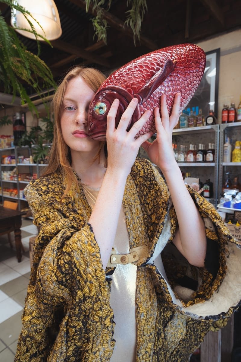 Woman in a gold brocade coat holding a red fish mask to her face, Rebecca Steinhofel (@rebecca_steinhofel), Viviers Studio, styling Laura Cooney