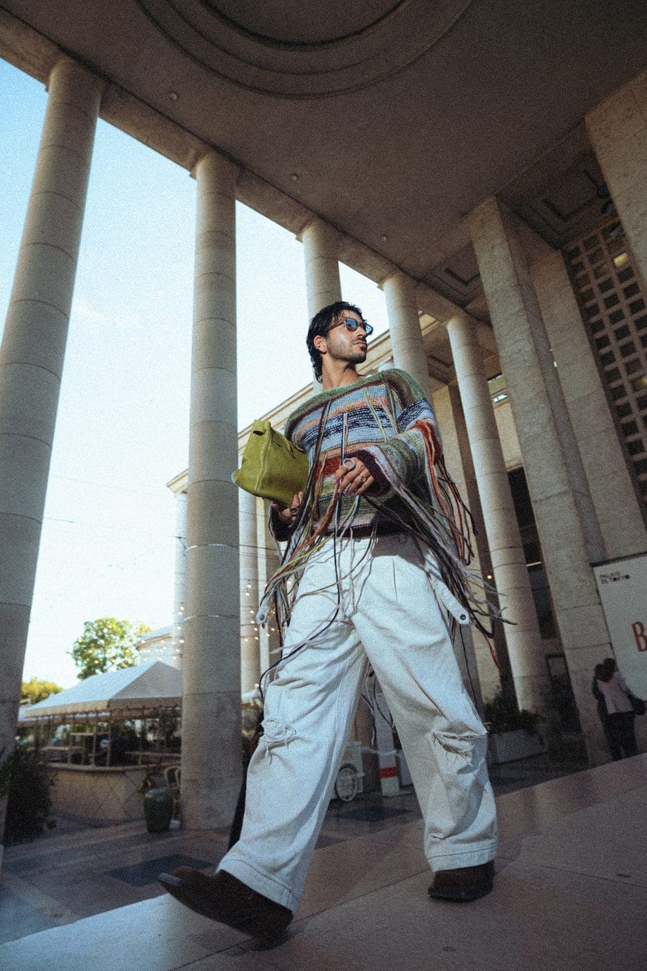 Man in a patterned knit and wide white jeans walking under a colonnade, Olaf Hernandez (@casoperdido)