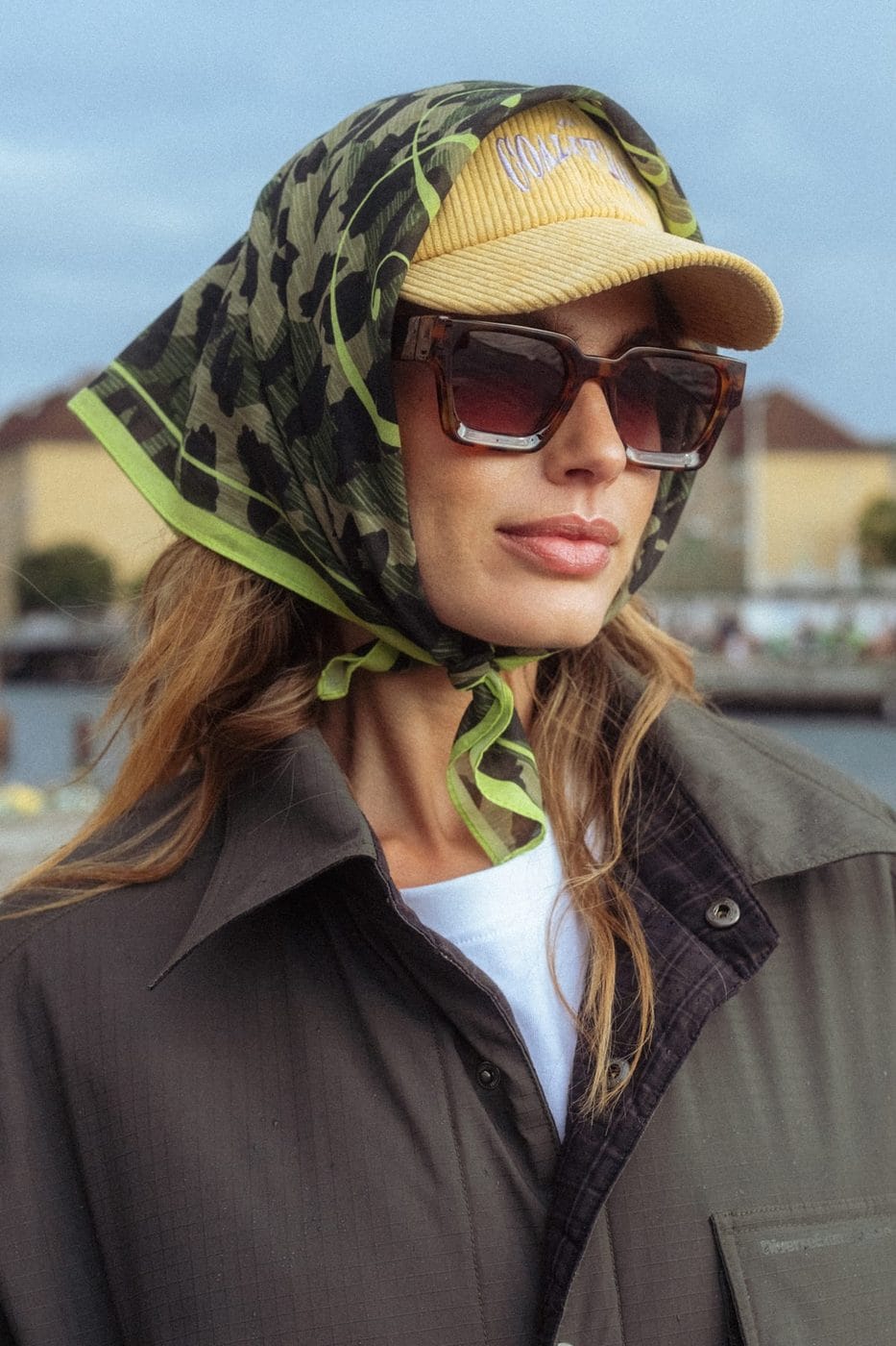 Portrait of a woman in a green leopard headscarf, yellow cap and sunglasses by the Seine
