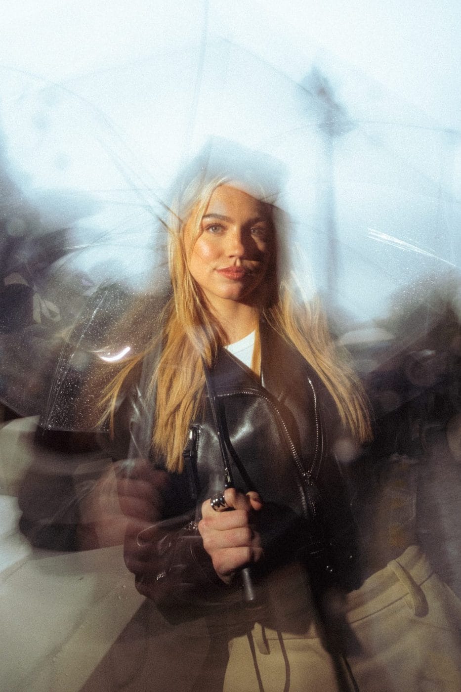 Blonde woman in a leather jacket seen through a blurred layered reflection, Emma Brooks (@emmabrooks)